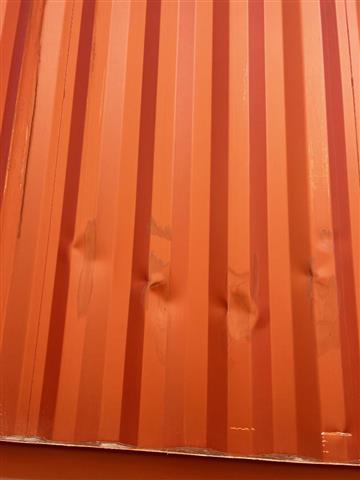 Orange corrugated container wall with visible dent damage